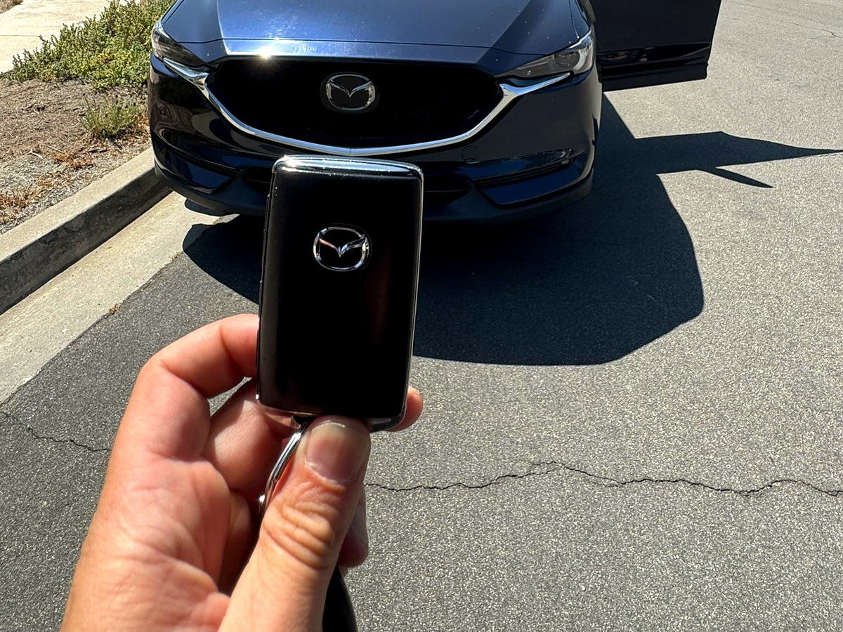 G.D. Locksmith technician holding the customer's Mazda smart key beside their car with the driver's door open in San Diego